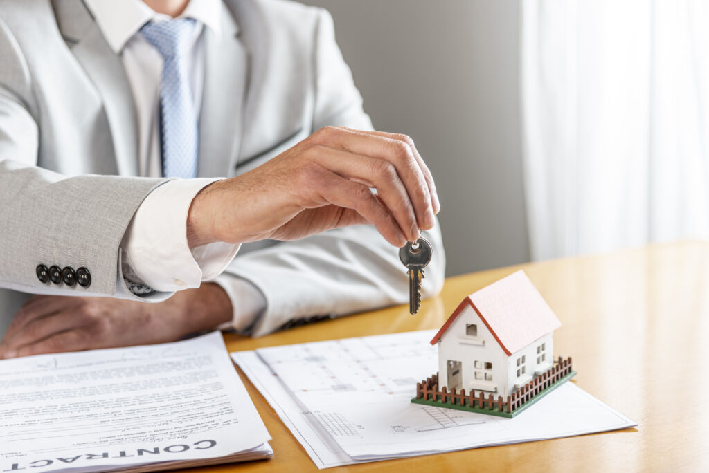 person-holding-house-keys-toy-model-house-desk